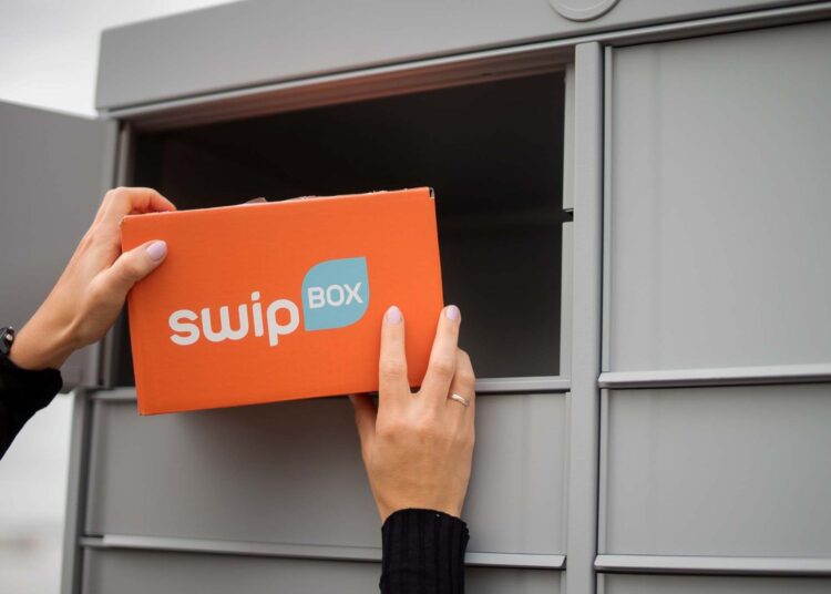 PostNord wprowadza w Finlandii automaty SwipBox, pomarańczowa tekturowa paczka wkładana do automatu paczkowego, męskie dłonie