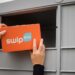 PostNord wprowadza w Finlandii automaty SwipBox, pomarańczowa tekturowa paczka wkładana do automatu paczkowego, męskie dłonie